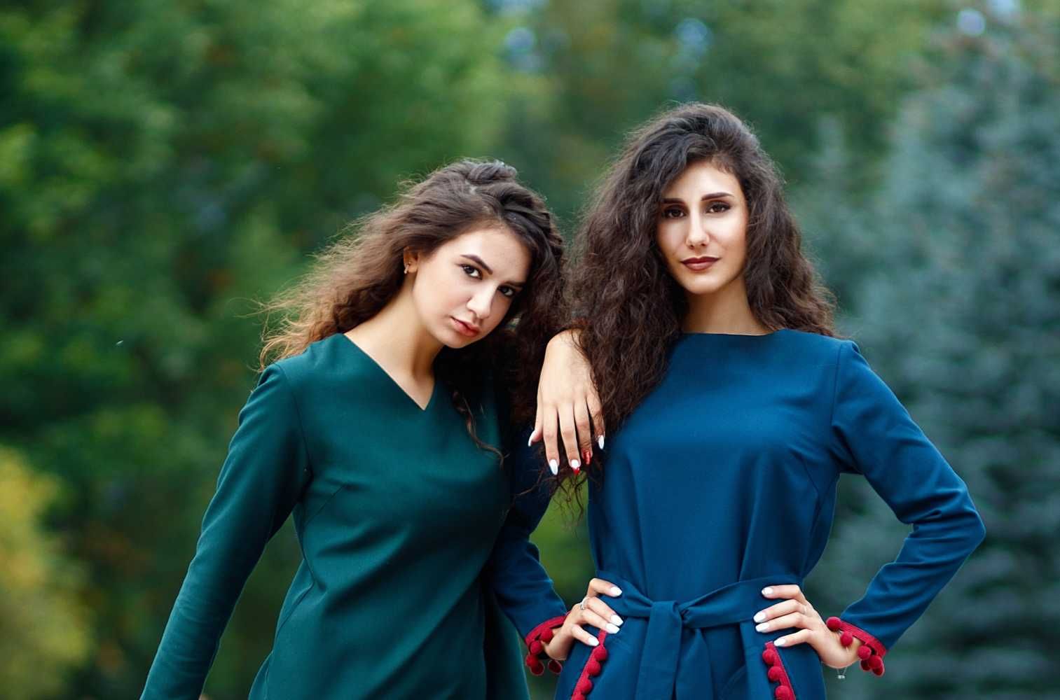 Photo of two co-founders in blue and green dresses with long brown hair staring at the camera.